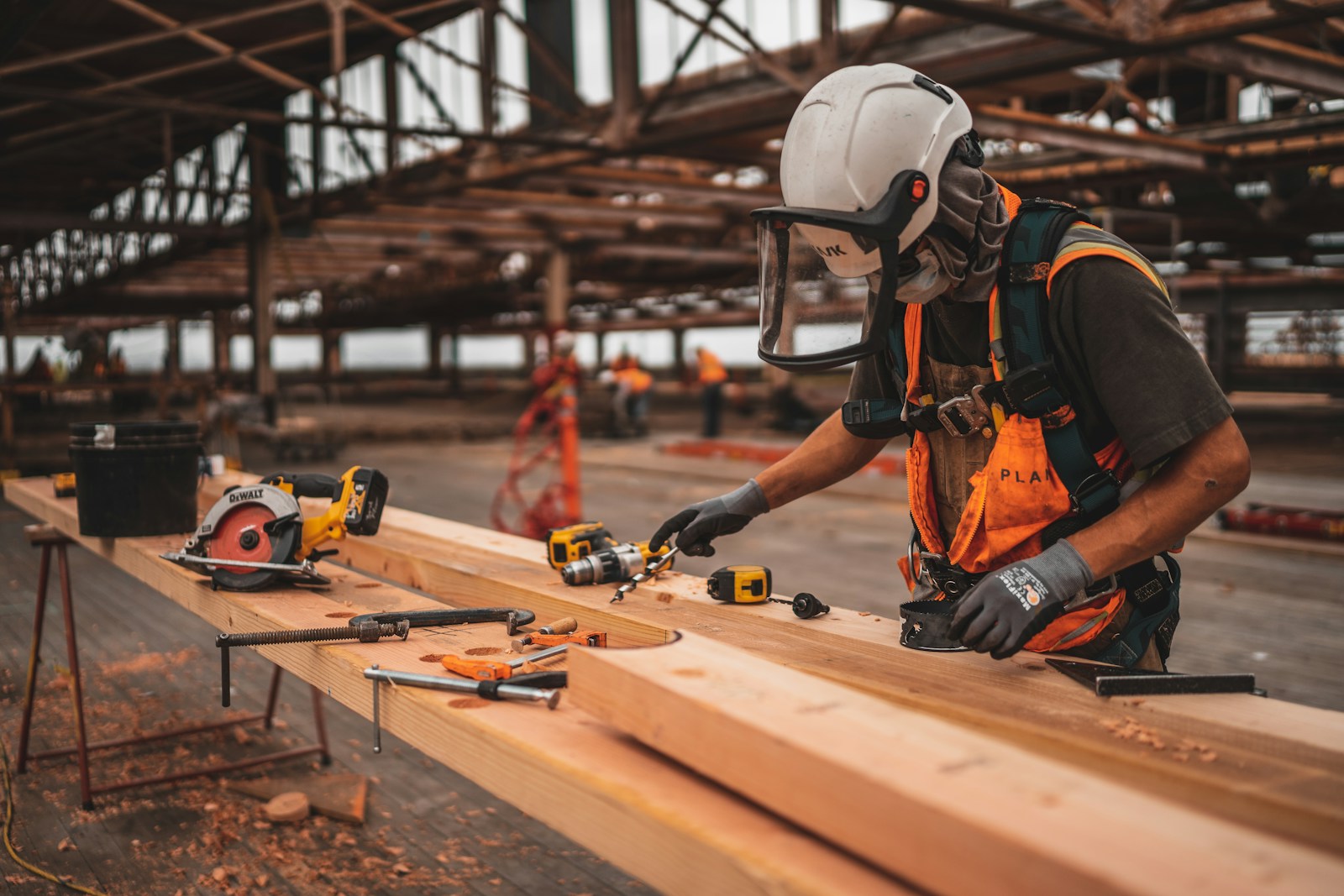 man in orange and black vest wearing white helmet holding yellow and black power tool artisan contractor